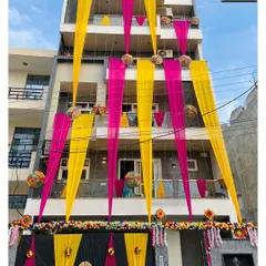 A full view of a house decorated for a wedding. The combination of bright pink and yellow drapes, along with traditional hangings, announces the celebration to the whole neighborhood.