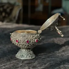 The silver kumkum box is shown open, revealing the container inside. The intricate carving on the base and the fine details of the hinged lid showcase its excellent craftsmanship.