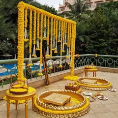 A beautiful poolside Haldi ceremony setup. The decor features a frame draped with yellow marigold garlands and traditional brass urlis for the ceremony, combining tradition with a resort-like feel.