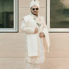 A full-length shot of the groom in his elegant white and gold sherwani, looking sharp and ready for his big day.