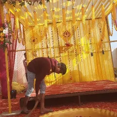 This photo shows my team at work, setting up a Haldi backdrop. We are arranging the yellow fabric and hanging marigold strings to create the perfect setting for the ceremony.