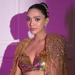 A portrait showing the front view of the look. The hair is styled in a severe, high bun, which complements the bold makeup and sequined gold outfit for a powerful editorial statement.