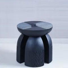 This sculptural accent table is carved from solid wood, with intricate textures on its legs and a patterned top. Its bold, architectural form and detailed craftsmanship make it a powerful statement piece that functions as both furniture and art.