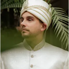 A classic portrait of the groom in his elegant white sherwani and turban. The natural, leafy background adds a touch of serenity to this handsome shot.
