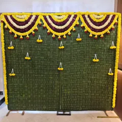 A unique and eco-friendly backdrop made of woven green leaves and decorated with marigold flower hangings, perfect for a traditional event.
