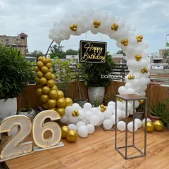 An elegant and modern 26th birthday setup on a rooftop terrace. This decoration features a stylish white and gold balloon semi-arch, large marquee light-up numbers, and a custom 'Happy Birthday' sign, perfect for a chic outdoor celebration.