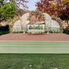 A chic and modern stage for a day wedding, featuring a white arched backdrop, lush floral decor, and a vintage-style sofa.