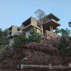 The raw concrete structure of our hillside project during construction, showing the bold, stacked volumes and cantilevered slabs. This image reveals the complex engineering required to build on a steep, forested slope.