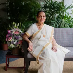 We also did some lifestyle portraits in her home, surrounded by lush greenery. This photo, with her in a classic white and gold saree, has a serene and natural feel, celebrating her in her own comfortable environment.