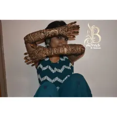 A playful shot of a bride showing off her full bridal mehndi, with detailed work on both her arms and feet.