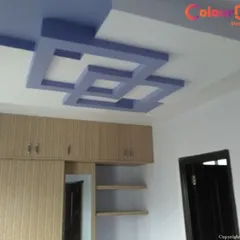 We created a bold statement in this bedroom with a custom geometric false ceiling. The intersecting blue and white POP structures add a modern, artistic touch and visual interest to the room, complementing the wooden cabinetry below.