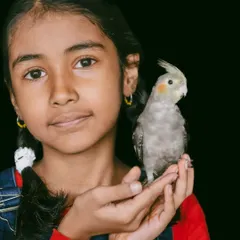 A lovely portrait of a young girl and her feathered friend. Her gentle hold and the bird's calm demeanor show a relationship built on trust and affection.