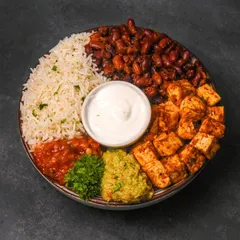 A colorful paneer burrito bowl with cilantro rice, kidney beans, salsa, guacamole, and sour cream, shot from above on a dark surface.
