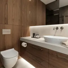 This bathroom showcases a custom vanity with a white countertop and wood-finish drawers. The wall-mounted toilet and fluted wood accent wall create a sleek, continuous look.