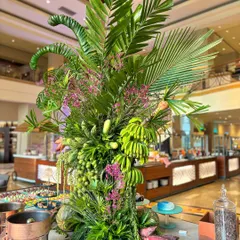 This nature inspired installation was designed to elevate a dining space. The arrangement is a vertical garden of green, featuring everything from gourds and bananas to palm leaves and delicate pink flowers, turning the buffet area into an adventure.