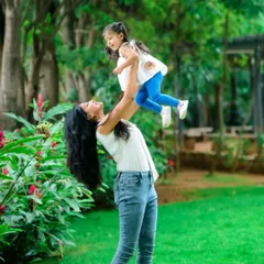 A beautiful, dynamic shot from a Mom & Me session in a park. The mother lifting her daughter into the air creates a sense of pure joy and freedom, a perfect candid moment.