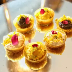 These bite-sized tartlets are filled with a variety of sweet creams and garnished with delicate rose petals. Served on a mirrored tray, their reflections create a beautiful and abundant display.