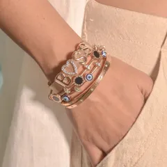 A powerful 'BOSS' bracelet stack. The personalized mesh band is the star, supported by complementary evil eye and studded bangles in a matching rose gold tone.