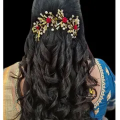 A beautiful half-up, half-down hairstyle with voluminous curls. This modern look is elevated with a stunning red and gold floral hair accessory, ideal for a reception or party.