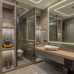 A modern bathroom design featuring large-format tiles, a floating vanity, and integrated linear LED lighting. The built-in, backlit shelving adds both storage and a soft, ambient glow.