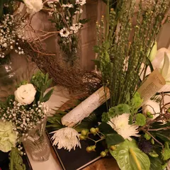 An overhead view of a rustic floral arrangement. We combined white chrysanthemums, baby's breath, and dried branches with antique-style paper scrolls to create a centerpiece with vintage charm.