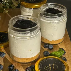 My Blueberry Cheesecake in a reusable glass jar. It features a crunchy biscuit base, a creamy cheesecake layer, and a generous topping of my homemade blueberry compote.