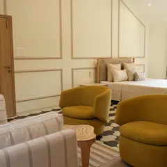 This wide view of the Alibaug master bedroom shows how we integrated a comfortable seating area. We upholstered the striped sofa and vibrant yellow chairs, which add a cheerful pop of color to the serene, neutral space.