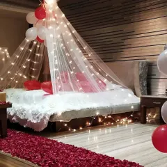 The details make the difference. Here, a beautiful canopy with fairy lights creates a cozy focal point over the bed, while a path of red rose petals on the floor adds a layer of classic romance to the room.