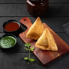This shot of samosas uses dramatic, directional lighting to emphasize their crispy, golden-brown texture. The dark background makes them the undisputed hero of the frame.