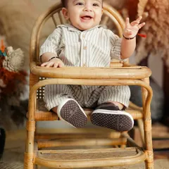 Celebrating six months of sweetness. This half-birthday shoot captures the baby's happy and expressive personality, sitting proudly in a miniature high chair in a boho-chic studio setup.