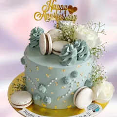 Celebrate your love with this stunning anniversary cake. It's decorated with fresh white roses, baby's breath, macarons, and delicate gold leaf flakes for a touch of luxury.