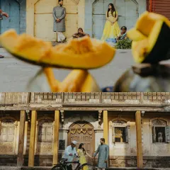 A creative street-level view of a pre-wedding shoot in the old city of Nashik, with a slice of pumpkin in the foreground framing the couple against a heritage 'wada'.