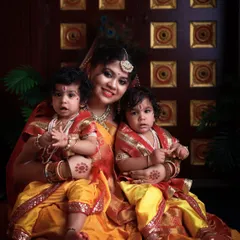 A mother's love multiplied by two. This beautiful portrait shows a mother in a traditional saree, lovingly holding her two young children who are dressed as little Krishnas for a festive shoot.