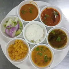 A deconstructed view of our South Indian meal plate. We offer regional cuisine options in our packed meals, including items like sambar, rasam, dal, and poriyal with rice.