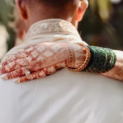 A beautiful shot of the bride's henna-stained hand, adorned with green bangles, resting on the groom's shoulder. The dark stain provides a stunning contrast and photographs beautifully.