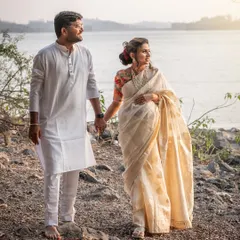 By the water's edge, this couple shares a quiet moment. The simplicity of their white traditional outfits against the serene landscape creates a powerful and soulful image of their bond.