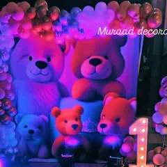 A close-up of a teddy bear themed first birthday stage. The backdrop features large teddy bears, complemented by dramatic blue and purple lighting and a light-up number '1'.