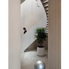 A view of the helical staircase from the side, showing how it carves a path through the space, complemented by a small indoor garden of white pebbles and greenery.