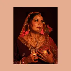 An artistic and moody portrait of a bride in her traditional red wedding lehenga. The use of a peacock feather and veil adds a layer of mystery and timeless beauty.
