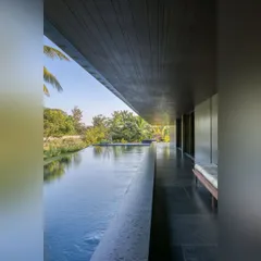 A long, linear infinity pool runs alongside the veranda of this Alibaug home. The dark stone and reflective surface mirror the sky and surrounding trees, making the pool an integral part of the landscape.