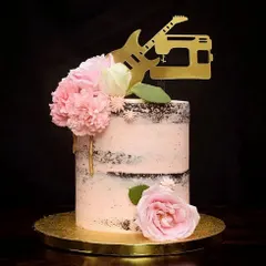 A rustic semi-naked wedding cake for a couple's special day. This design combines exposed chocolate cake layers with light pink buttercream, fresh flowers, and a custom topper reflecting the couple's hobbies of music and sewing.