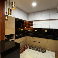 A perfect example of a premium acrylic kitchen. The design features a striking contrast between black and beige high-gloss laminates, complemented by a black granite countertop and elegant pendant lights over the breakfast counter.