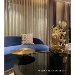 A detail shot of the Shanti Niketan lounge, highlighting the interplay of textures. The deep blue velvet of the sofa contrasts with the cool, reflective surface of the black glass coffee table and a sculptural golden accent piece.