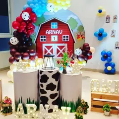 I designed this farmyard theme for a first birthday party. The centerpiece is a red barn backdrop with the child's name, surrounded by balloon arrangements and pedestals with cow-print details to match the farm animal theme.