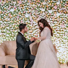 The groom gets down on one knee to propose during their engagement ceremony, against a stunning wall of pastel flowers. I help stage these unforgettable romantic gestures.