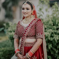 A bride's smile that lights up the room. This candid portrait captures her natural joy and radiance, showcasing her beautiful red lehenga and traditional jewelry in a soft, outdoor setting.
