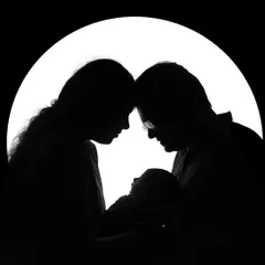Sometimes, the most powerful family portraits are the simple ones. This silhouette shot creates a timeless and emotional image, focusing on the bond between new parents and their baby against a clean, bright background.