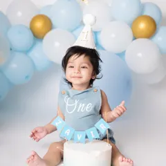 Here is Zavir, one half of the dynamic twin duo, looking absolutely charming before the cake chaos began. His custom 'One' romper and the beautiful blue balloon setup created the perfect scene for his first birthday milestone.