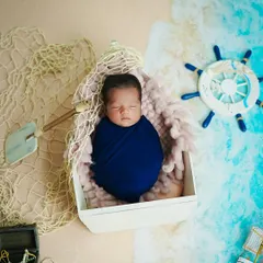 Our little sailor has arrived. This newborn is peacefully asleep in a boat-shaped prop, surrounded by a nautical theme with a ship's wheel, fishing net, and treasure chest. It's a creative way to announce your new arrival.