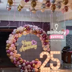 Celebrating a silver anniversary with a touch of glamour. This indoor setup includes a stunning balloon ring in pink and metallic tones, a "Happy Anniversary" neon sign, and bold, illuminated "25" marquee numbers.